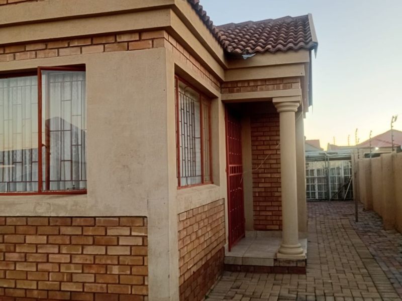 A well-maintained face brick house exterior featuring a paved walkway, secure entrance with security gate, and classic tiled roof architecture.