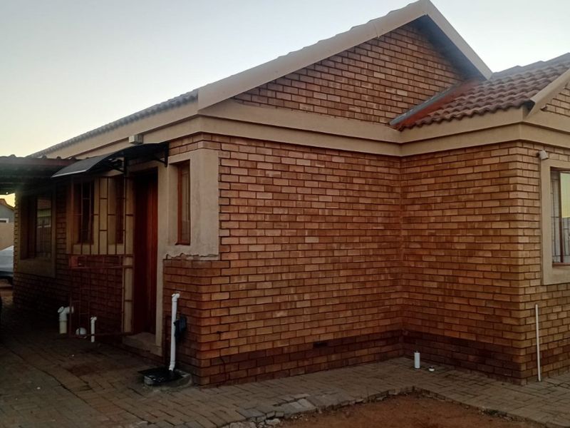Rear view of a face brick house featuring a tiled roof, paved walkway, and external plumbing fixtures.