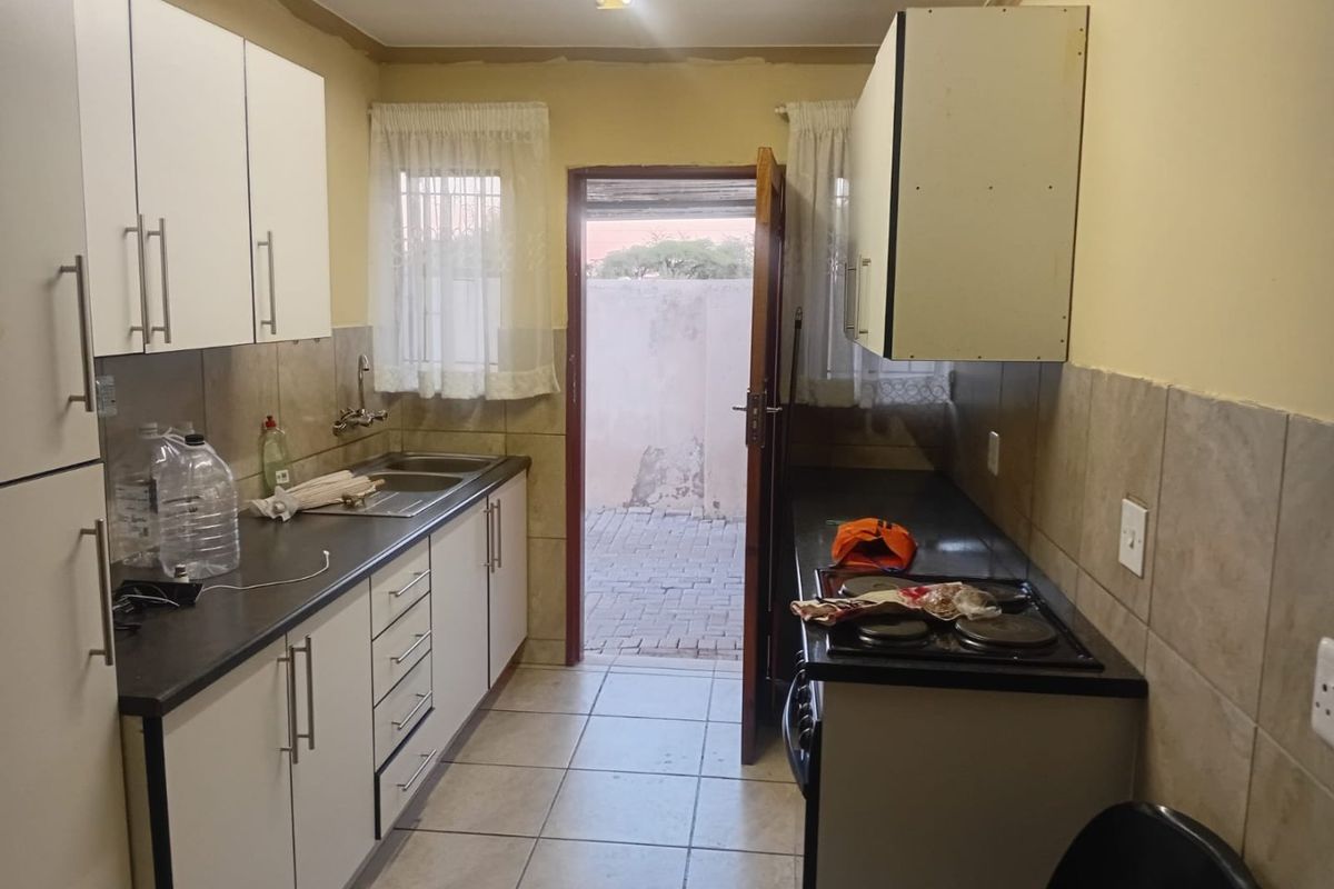 A functional galley-style kitchen featuring white cabinetry, dark countertops, an electric hob, and direct access to an outdoor area.