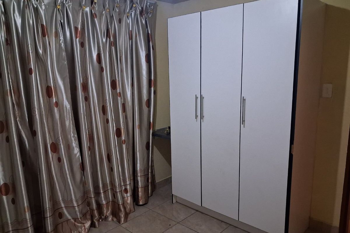 A bedroom featuring tiled flooring and a modern white built-in wardrobe with silver handles.