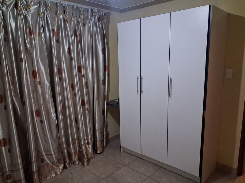A bedroom featuring tiled flooring and a modern white built-in wardrobe with silver handles.