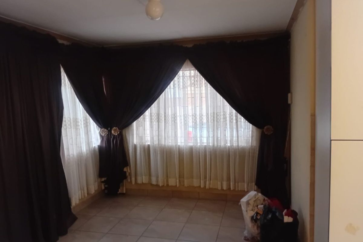 An empty living area featuring tiled flooring and a large corner window, currently awaiting cosmetic updates and finishing touches.
