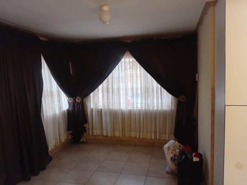 An empty living area featuring tiled flooring and a large corner window, currently awaiting cosmetic updates and finishing touches.