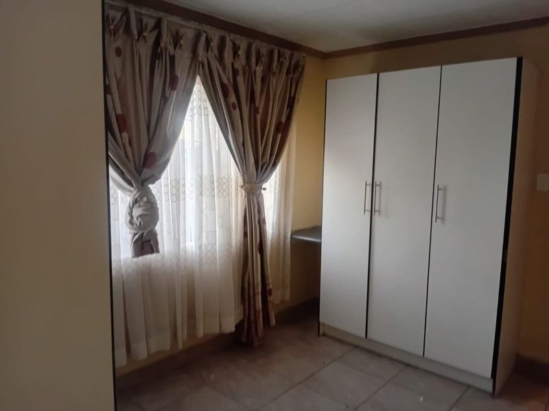 A bedroom featuring tiled flooring and a built-in white wardrobe, offering functional storage space.