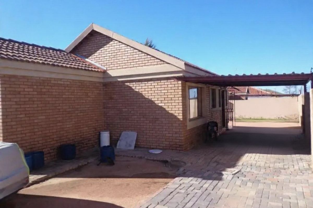 Rear view of the property featuring a face brick facade, tiled roof, and a paved driveway with an attached carport structure.