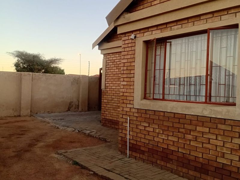 A view of the rear exterior featuring face brick construction, a paved walkway, and a perimeter boundary wall.
