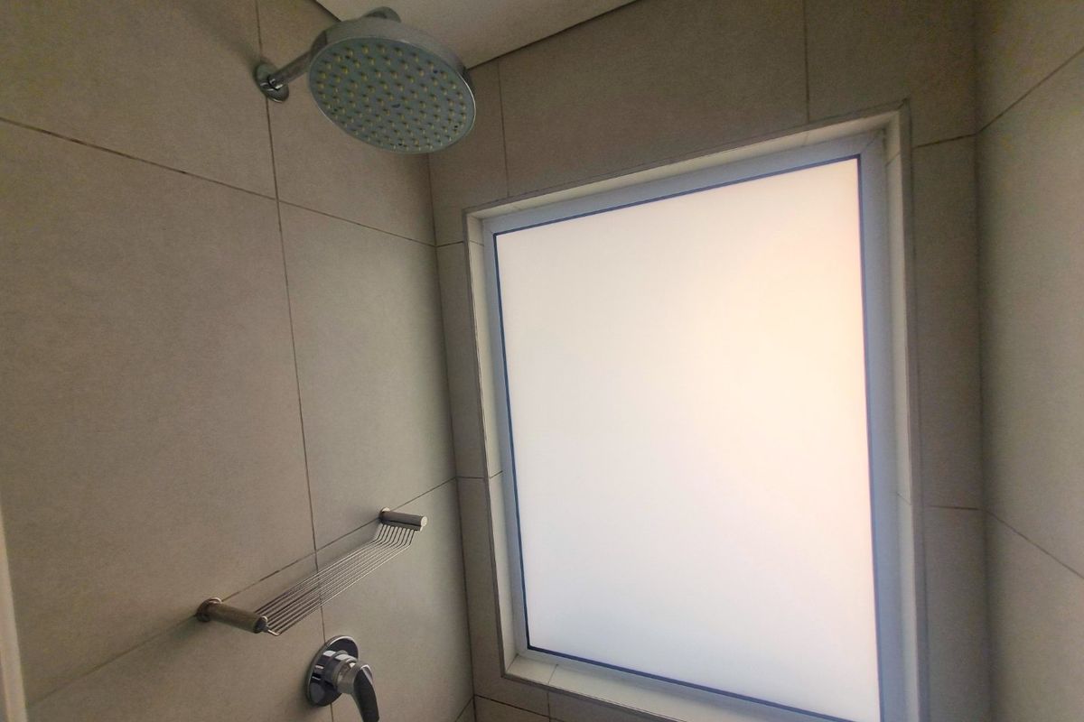 A clean, modern shower enclosure featuring neutral wall tiles, a fixed shower head, mixer tap, and a frosted glass window for privacy.
