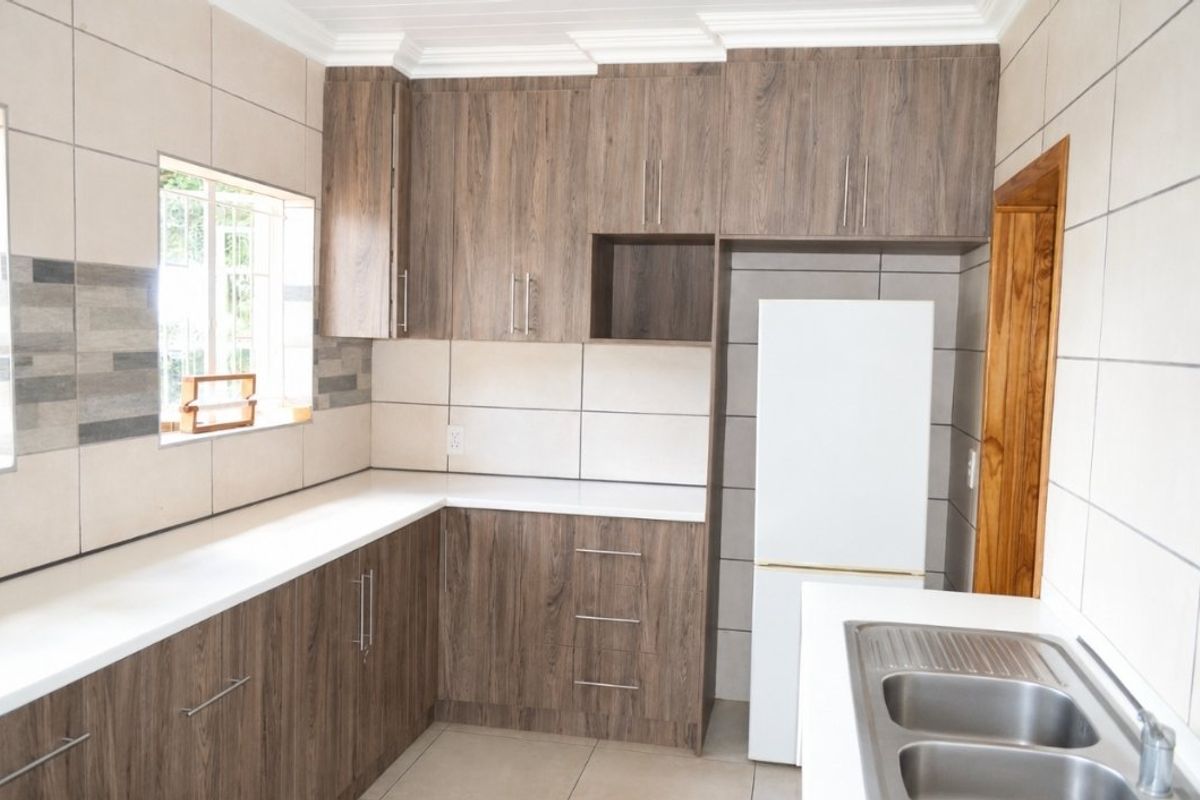 Modern kitchen featuring wood-look cabinetry, white stone countertops, a double stainless steel sink, and neutral tiled splashbacks.
