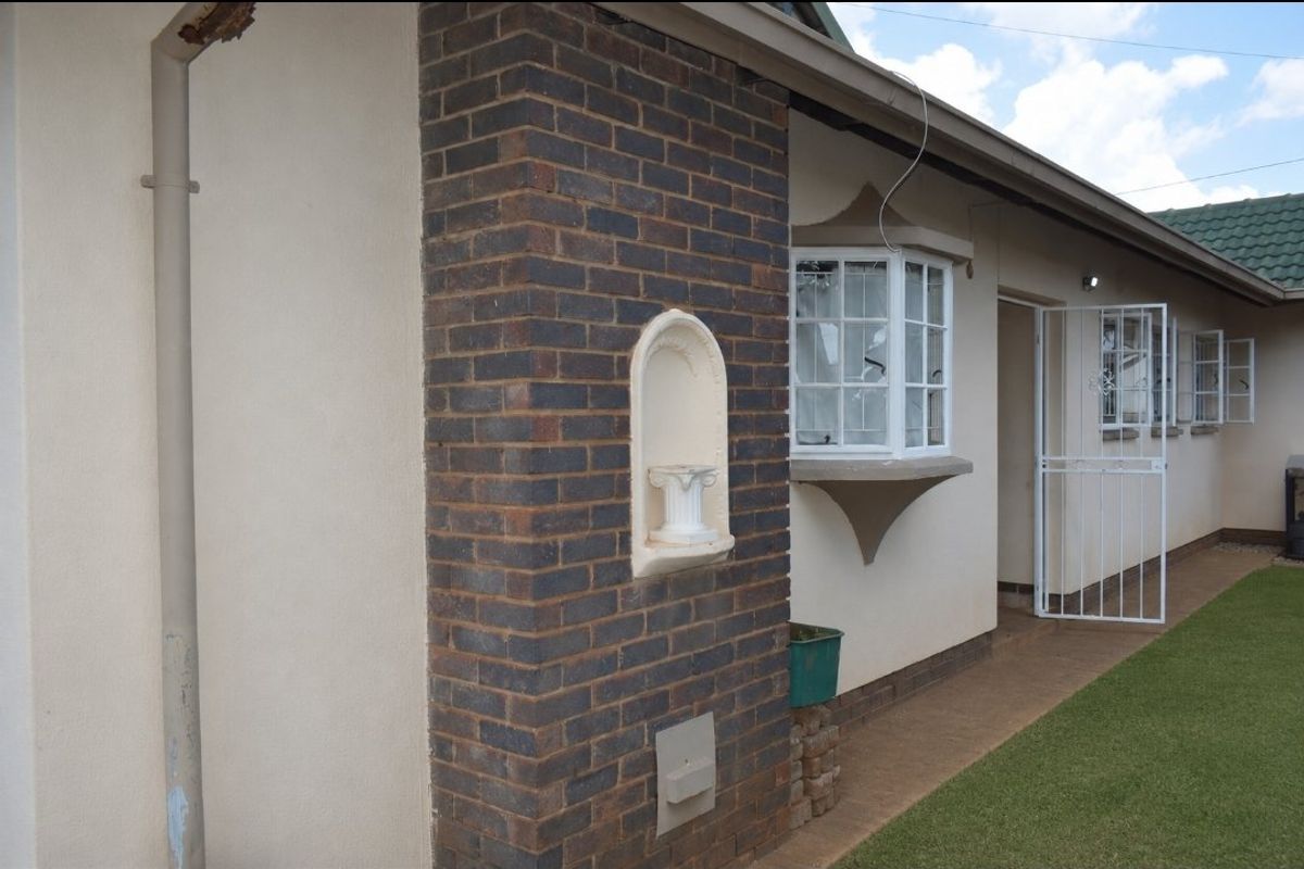 Side view of the property featuring a brick facade, bay window, and security gate access to the rear garden area.