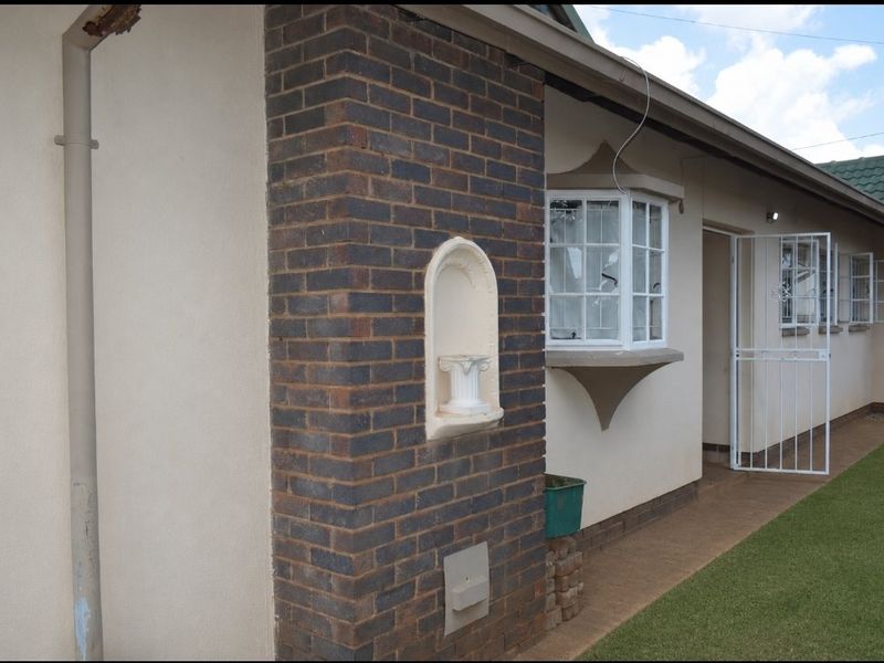 Side view of the property featuring a brick facade, bay window, and security gate access to the rear garden area.