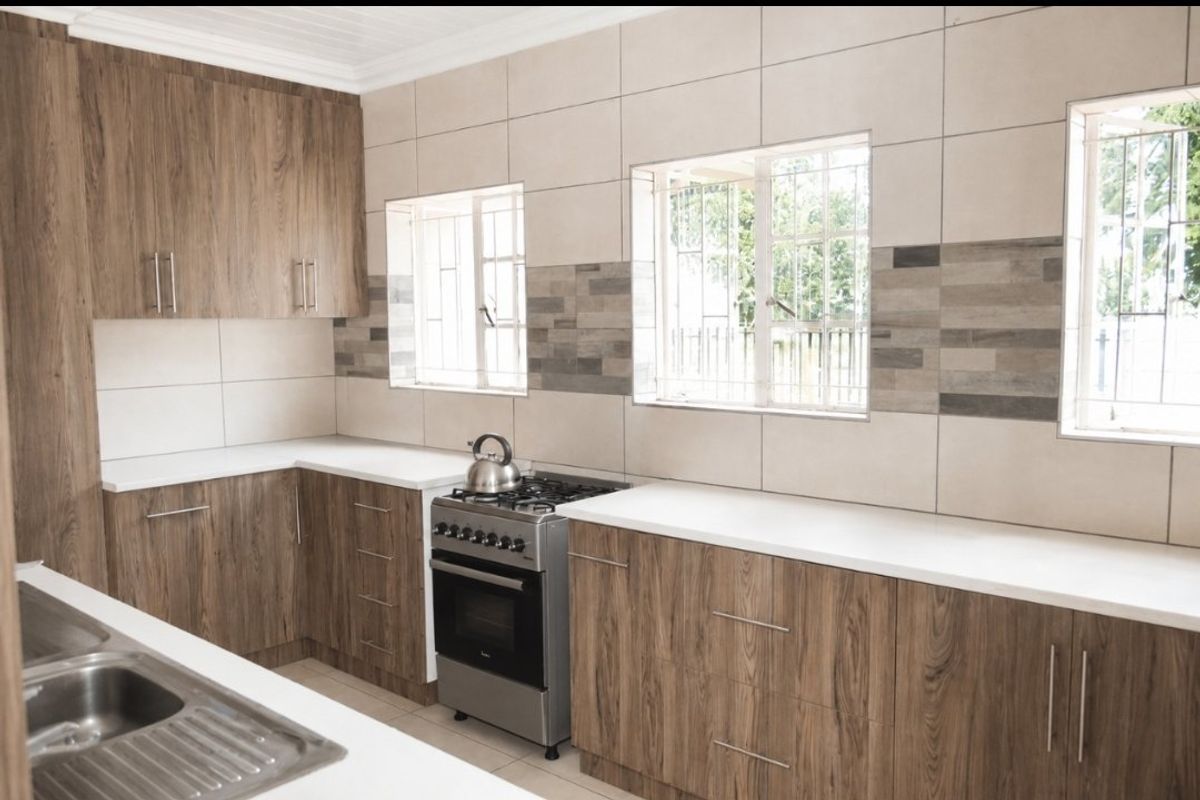 Modern kitchen featuring wood-look cabinetry, white stone countertops, a stainless steel freestanding stove, and a tiled backsplash with integrated sink.