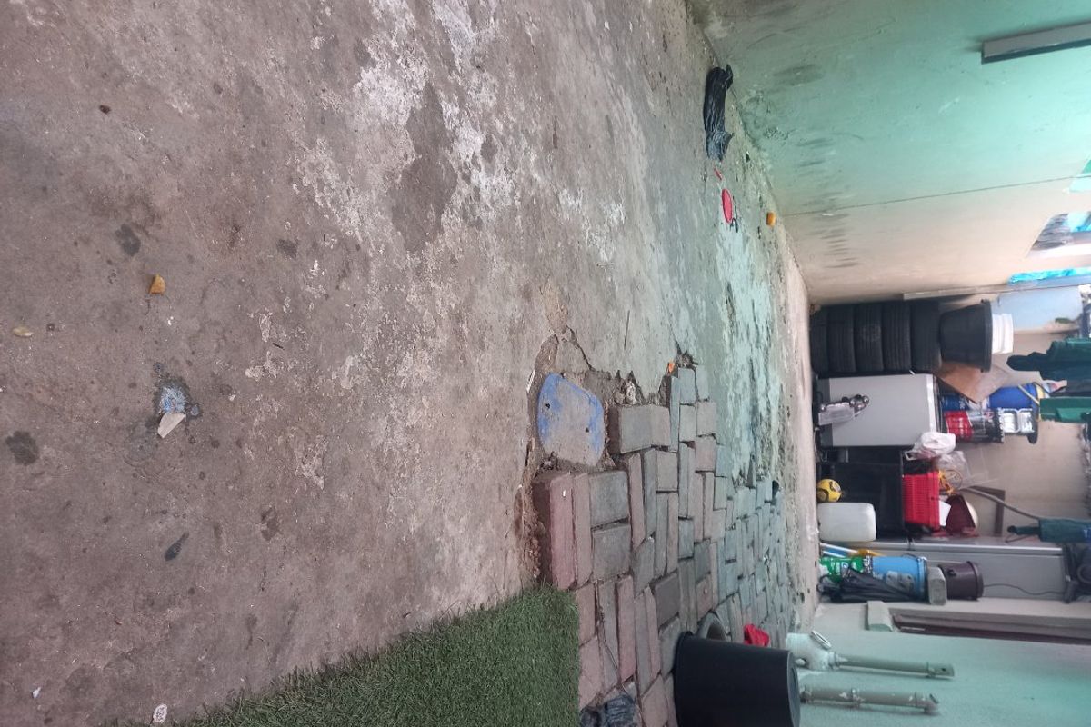 A rear exterior area featuring a mix of concrete and brick paving, showing significant wear and surface deterioration.