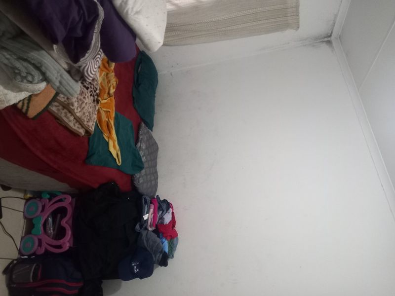 A bedroom interior featuring plain walls and ceiling with visible signs of surface staining and discoloration in the corner.