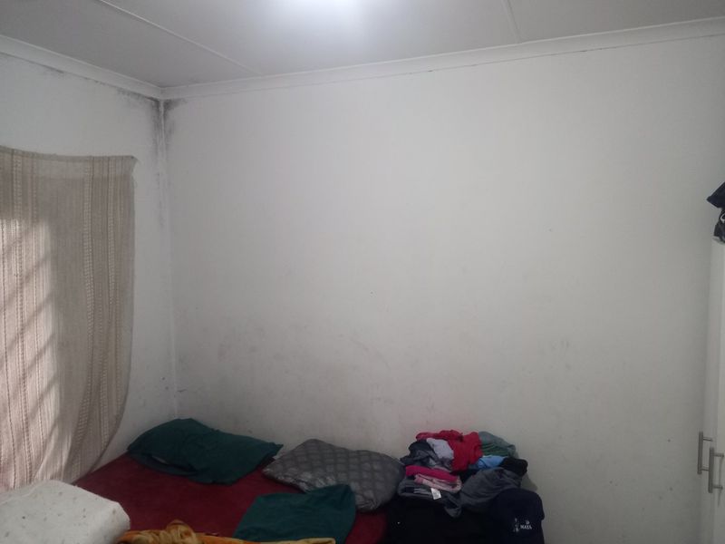 A bedroom featuring a built-in wardrobe, currently showing signs of wall staining and damp marks in the corner requiring maintenance.