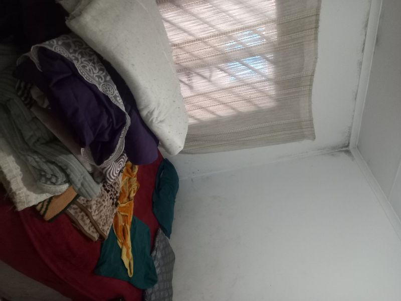 A bedroom interior featuring security bars on the window and visible signs of moisture damage on the ceiling and wall corners.