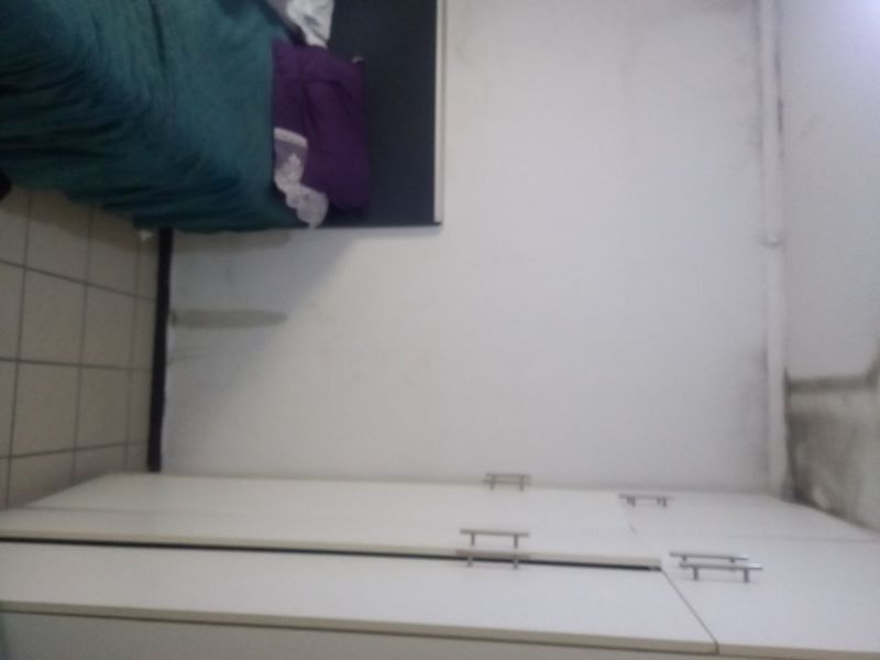A bedroom featuring built-in cupboards and tiled flooring, showing signs of wall and ceiling staining requiring maintenance.