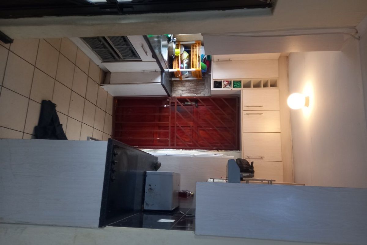 A compact kitchen featuring built-in cabinetry, a hob, and tiled flooring, with a security gate leading to the exterior.