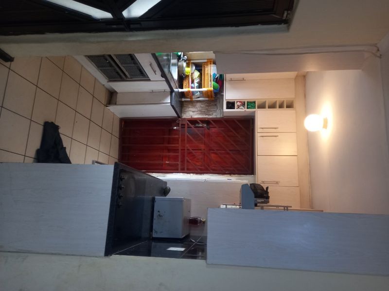 A compact kitchen featuring built-in cabinetry, a hob, and tiled flooring, with a security gate leading to the exterior.