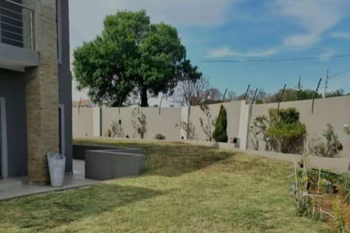 A spacious rear garden featuring a well-maintained lawn, perimeter wall with electric fencing, and a stone-clad pillar supporting an upper-level balcony.