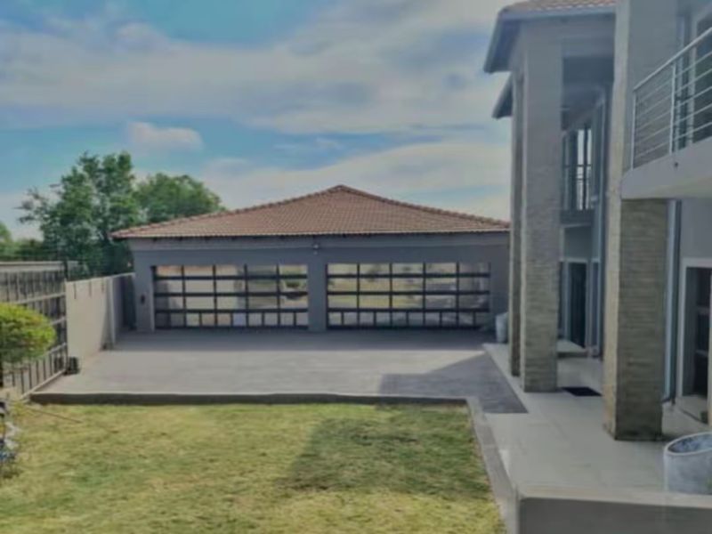 Rear view of the property featuring a double garage with glass panel doors, a paved driveway, and a multi-story structure with a balcony.
