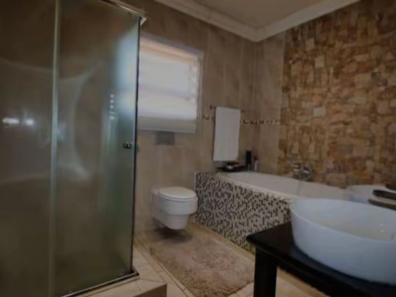 A well-appointed bathroom featuring a glass shower enclosure, wall-mounted toilet, built-in bathtub, and a decorative stone feature wall.