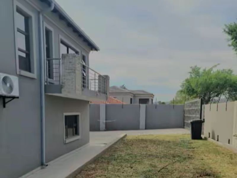 Rear view of the property featuring a balcony, paved walkway, and perimeter wall with a metal gate.