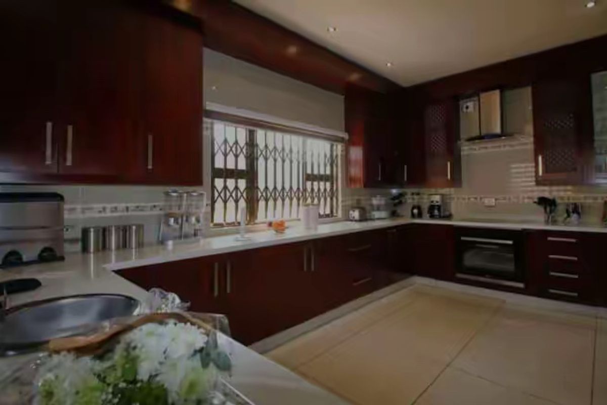 A spacious kitchen featuring dark wood cabinetry, stone countertops, built-in oven, extractor fan, and tiled flooring with security bars on the window.