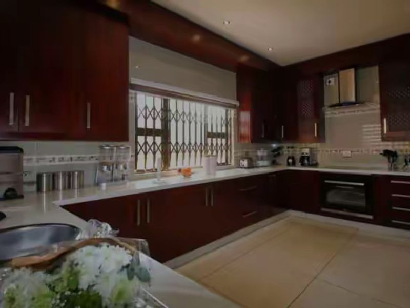 A spacious kitchen featuring dark wood cabinetry, stone countertops, built-in oven, extractor fan, and tiled flooring with security bars on the window.