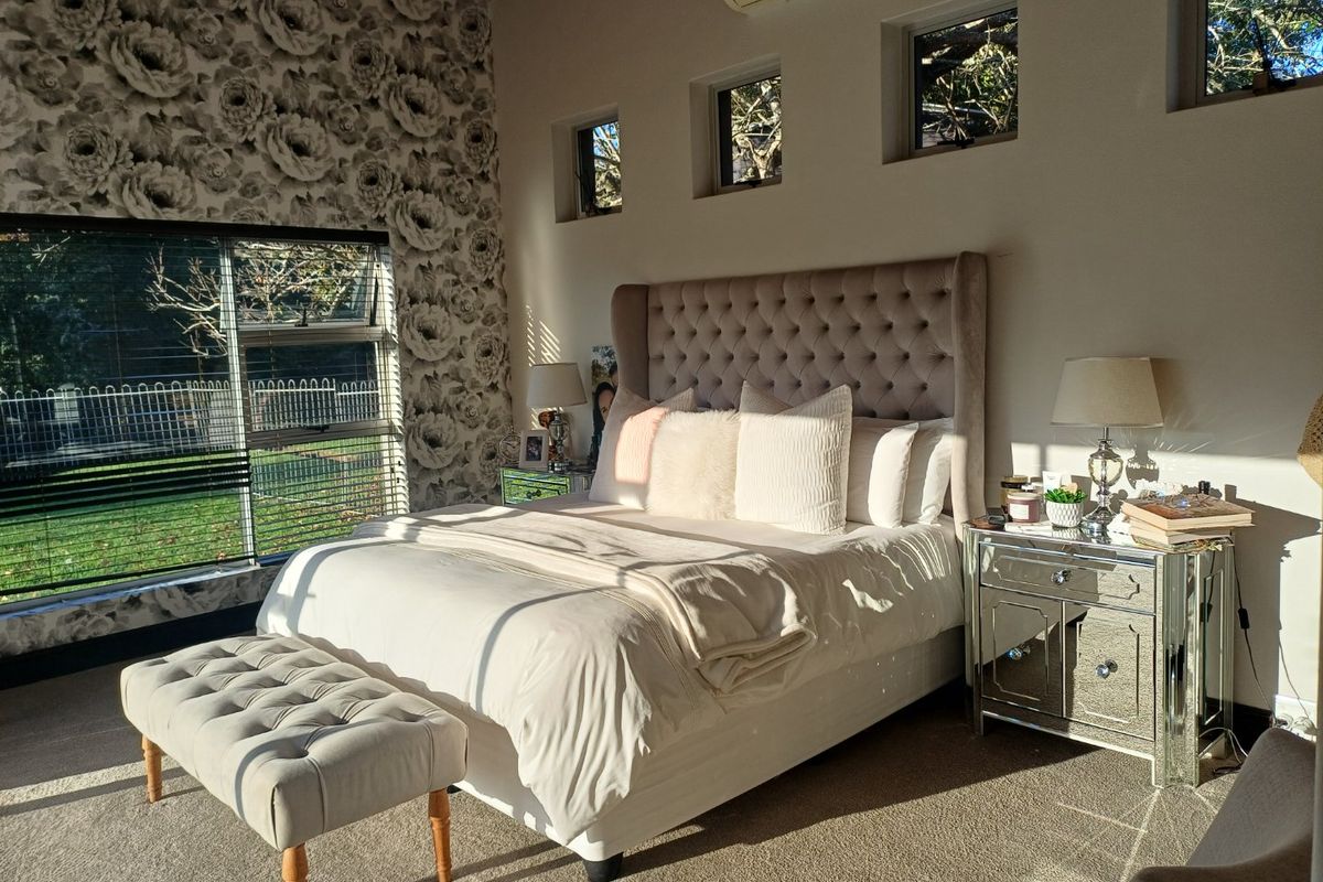 A well-lit bedroom featuring a large picture window, high timber ceilings, and multiple clerestory windows, creating a bright and airy atmosphere.