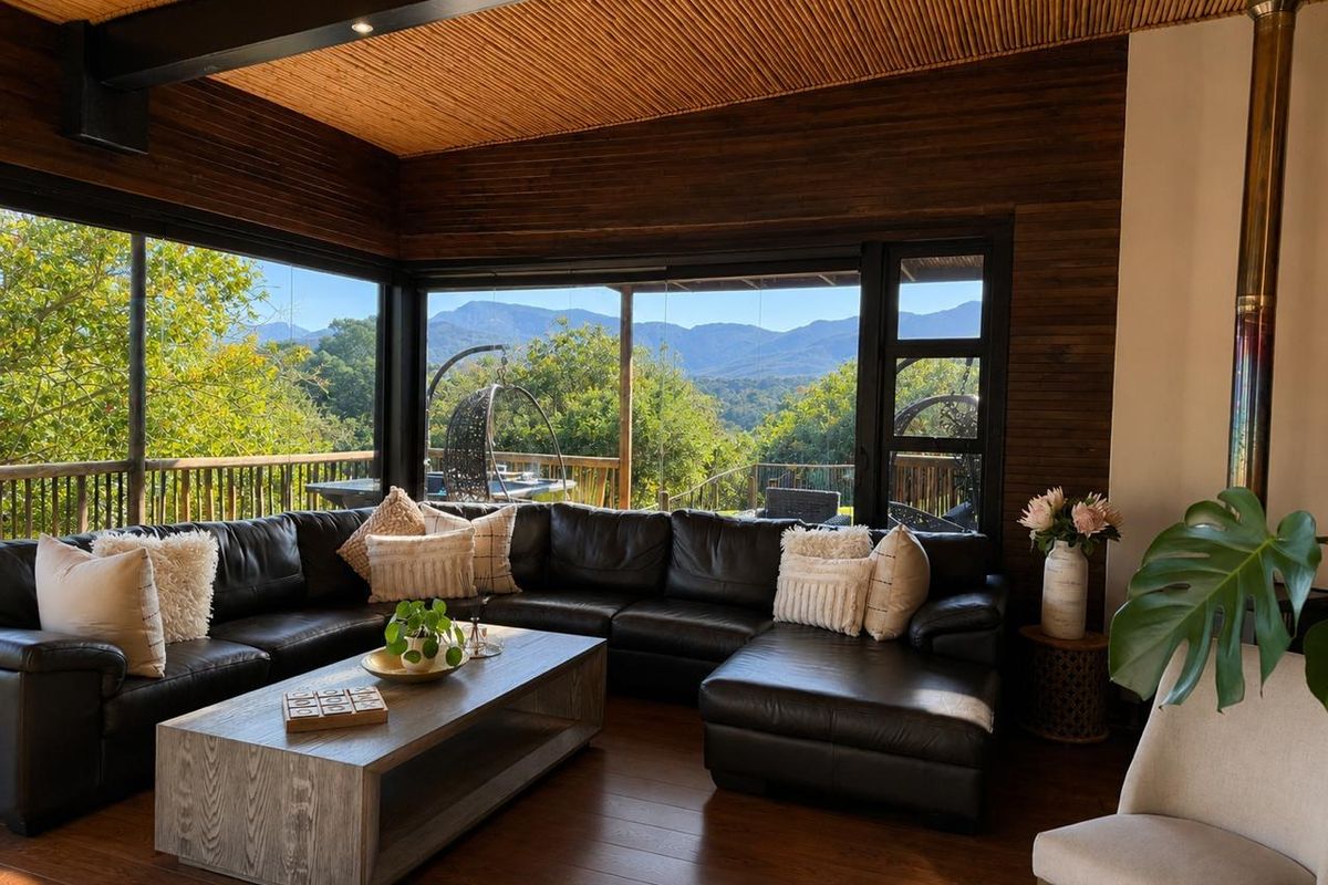 Elegant living room featuring a timber-clad ceiling, hardwood floors, and expansive corner windows offering panoramic mountain views, complemented by a built-in wood-burning fireplace.