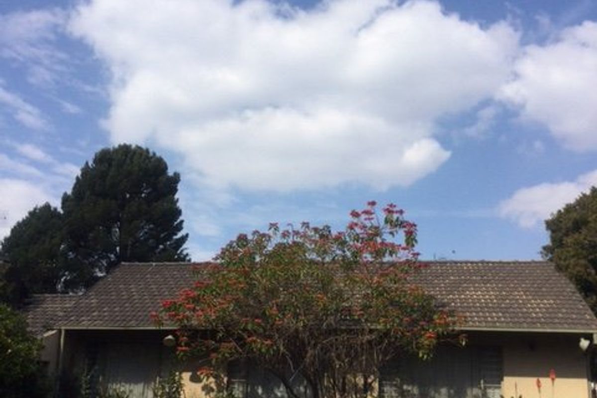 Rear view of the house featuring a tiled roof, brick exterior walls, and security shutters overlooking a garden area.