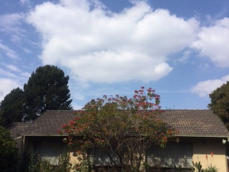 Rear view of the house featuring a tiled roof, brick exterior walls, and security shutters overlooking a garden area.