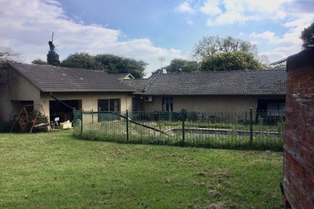Rear view of the property featuring a swimming pool with metal fencing, tiled roof, and sliding glass doors leading to the garden area.