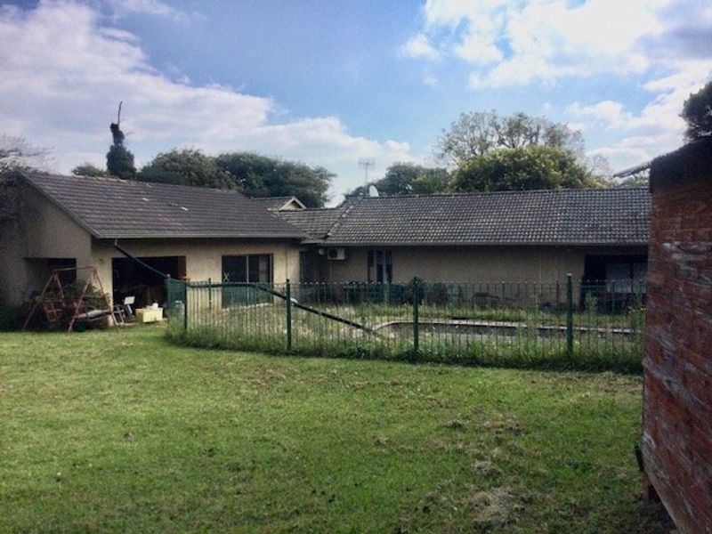 Rear view of the property featuring a swimming pool with metal fencing, tiled roof, and sliding glass doors leading to the garden area.