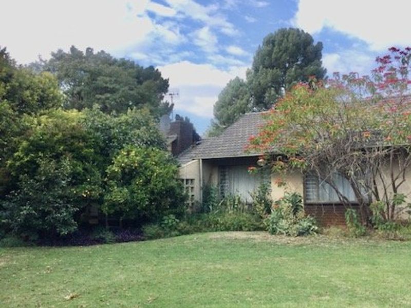 A view of the rear garden and house exterior, featuring a lawn, mature landscaping, and a tiled roof structure.