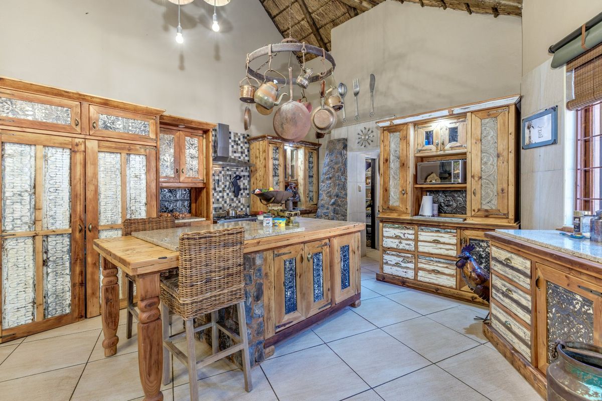 Rustic farmhouse kitchen featuring custom timber cabinetry, stone-clad island with granite countertop, tiled flooring, and a high thatched ceiling.