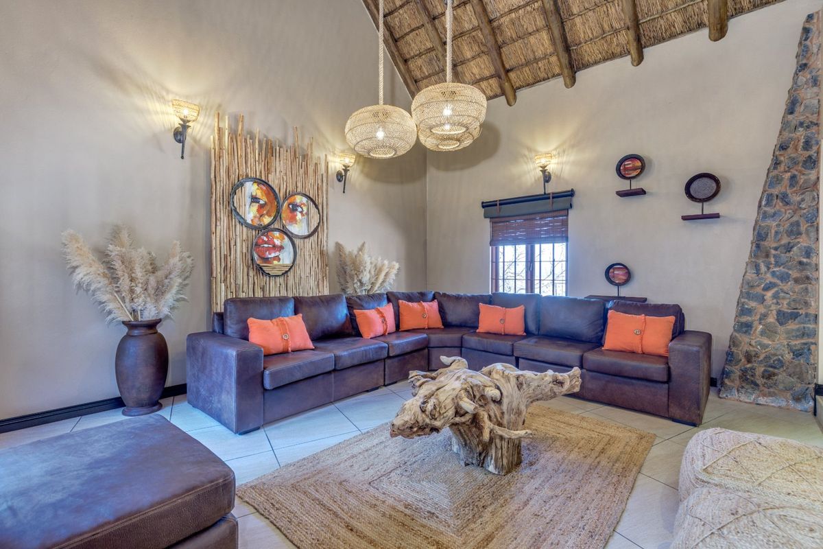 Spacious living room featuring a high vaulted thatched ceiling with exposed timber rafters, tiled flooring, and a rustic stone fireplace.
