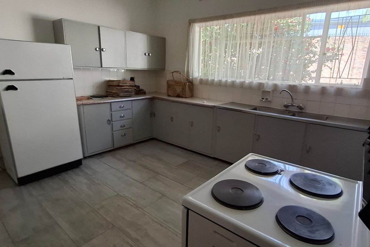 A functional kitchen featuring original cabinetry, a tiled countertop, a stainless steel sink, and an electric stove with tiled flooring.