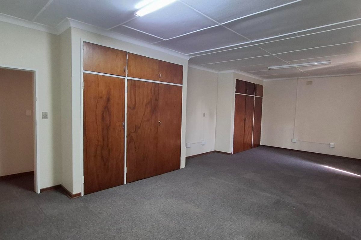 Spacious bedroom featuring extensive built-in wooden cupboards, carpeted flooring, and an integrated air conditioning unit.