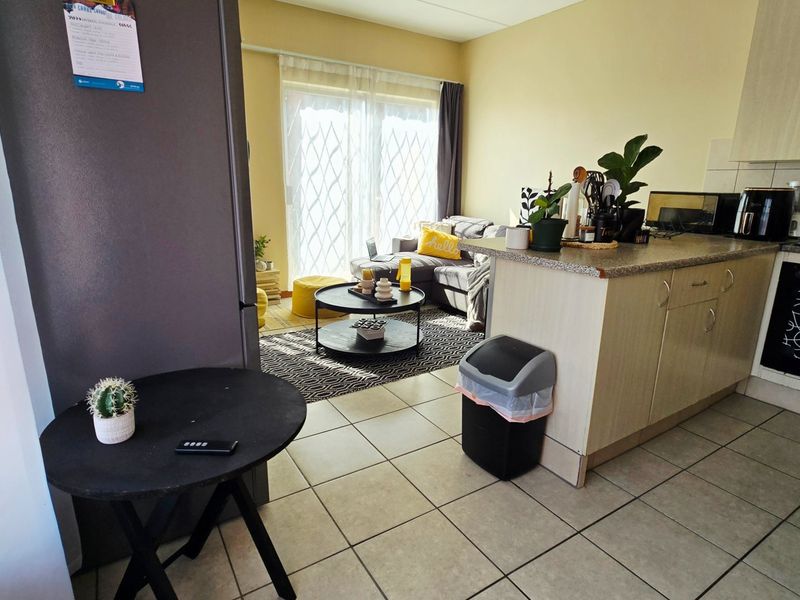 Open-plan living area featuring a functional kitchen with built-in cabinetry and tiled flooring, seamlessly connecting to a bright lounge with sliding door access.