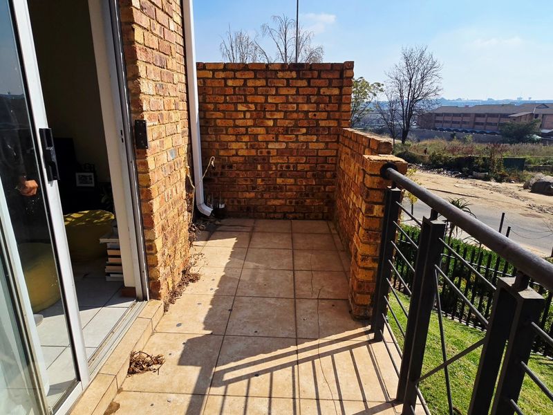 A private balcony featuring face brick walls, tiled flooring, and a metal balustrade, offering an outdoor space accessible via a sliding glass door.