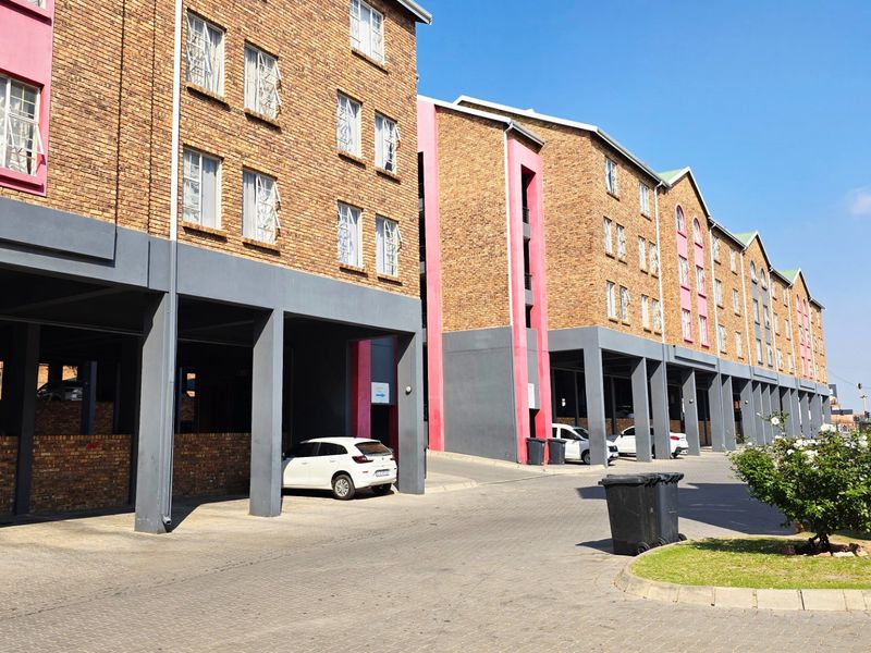 Exterior view of a multi-story apartment complex featuring face brick facades, covered ground-level parking, and paved driveway access.