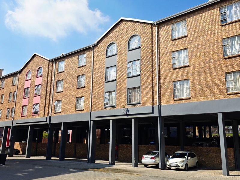A multi-story apartment building featuring a classic brick facade, arched windows, and a ground-level covered parking area with concrete support pillars.