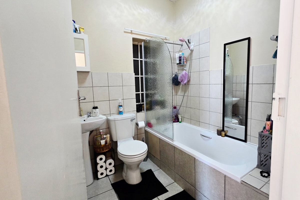 A functional bathroom featuring a pedestal basin, toilet, and a bathtub with a glass shower screen, finished with neutral wall and floor tiling.