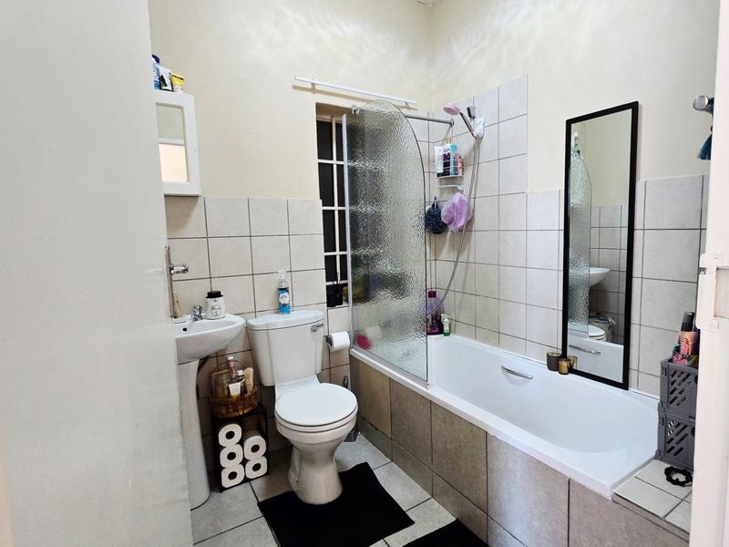 A functional bathroom featuring a pedestal basin, toilet, and a bathtub with a glass shower screen, finished with neutral wall and floor tiling.