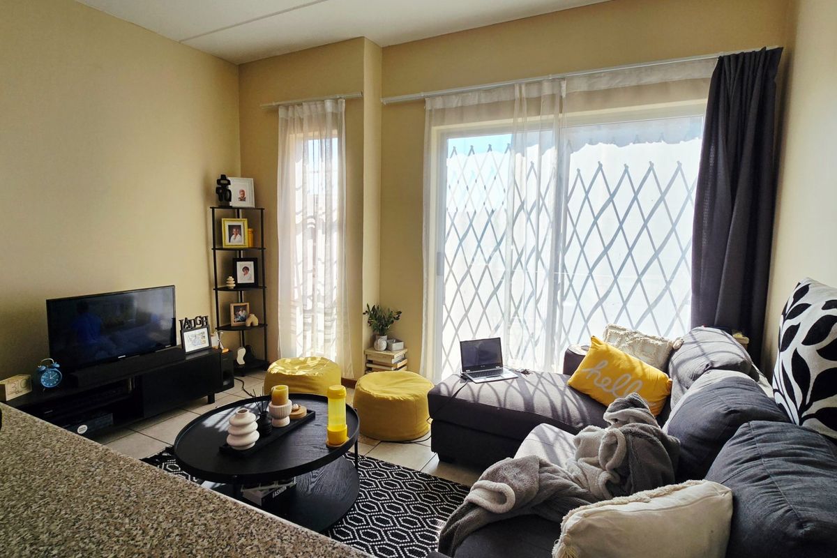 A comfortable living room featuring tiled flooring and a large sliding glass door with an integrated security gate, providing access to the outdoors.