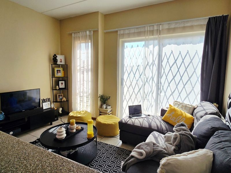 A comfortable living room featuring tiled flooring and a large sliding glass door with an integrated security gate, providing access to the outdoors.