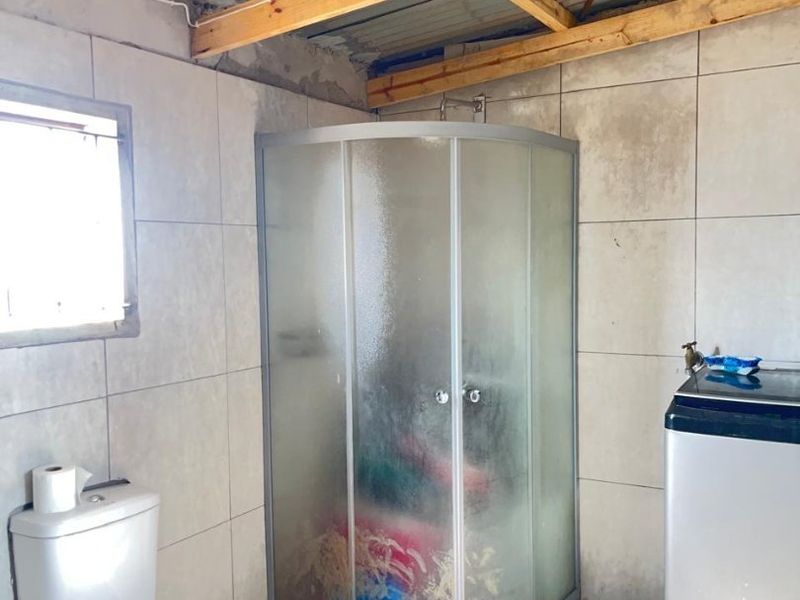 A functional bathroom featuring a corner shower enclosure, toilet, and tiled finishes, currently requiring cosmetic updates and ceiling completion.