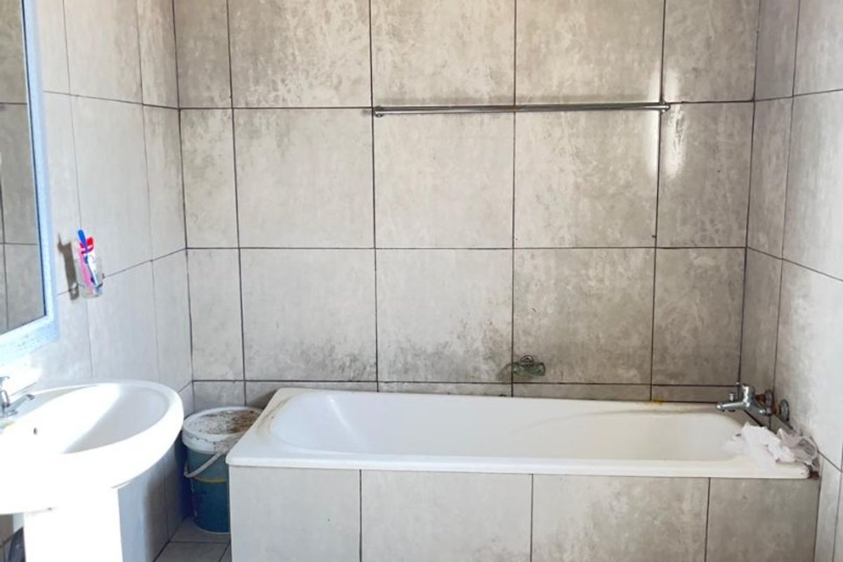 A basic bathroom featuring a pedestal basin, built-in bathtub, and tiled finishes, currently requiring ceiling completion and general refurbishment.