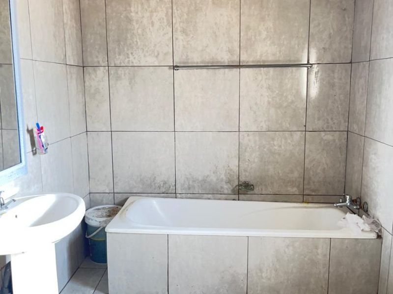 A basic bathroom featuring a pedestal basin, built-in bathtub, and tiled finishes, currently requiring ceiling completion and general refurbishment.